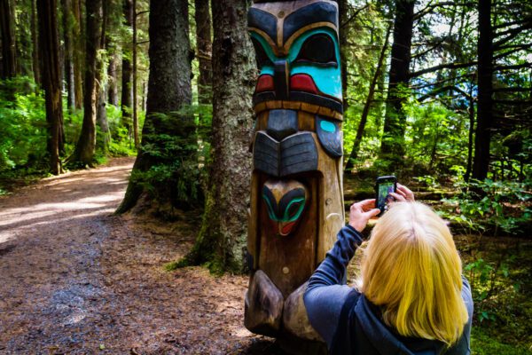 Woman taking a photo of a totem pole in Sitka National Historical Park